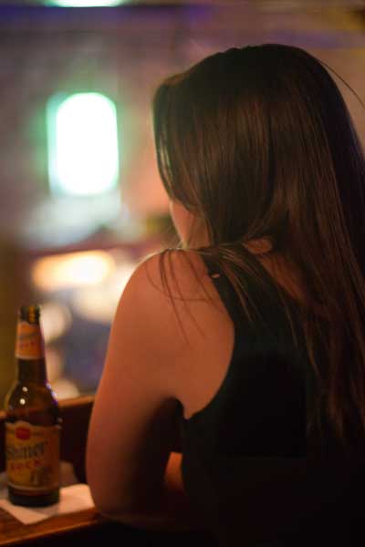 Woman sitting at bar with Shiner beer, overlooking band below