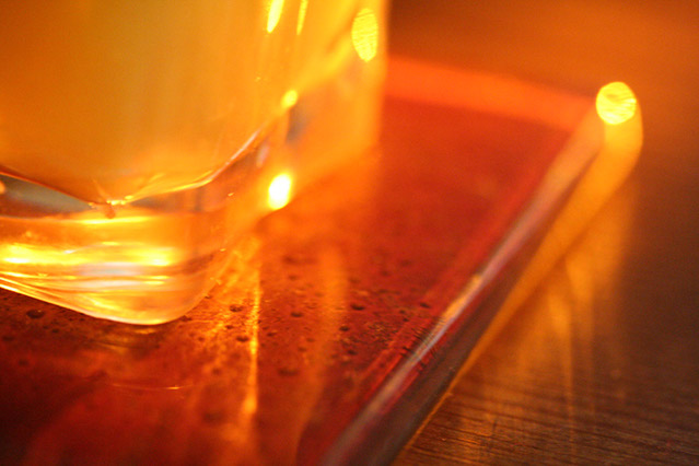 Glass of orange juice sitting on red tile coaster and  lit by a beam of sunlight.